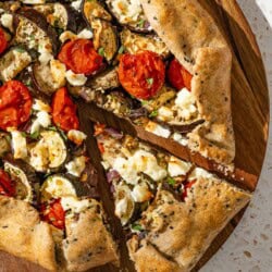 An overhead photo of a savory galette with one slice cut from it on a wooden serving board.