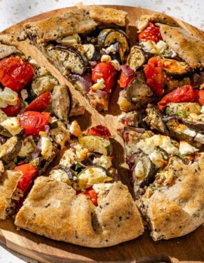 A close up of a savory galette cut into slices on a wooden serving board.