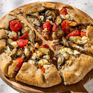 A close up of a savory galette cut into slices on a wooden serving board.