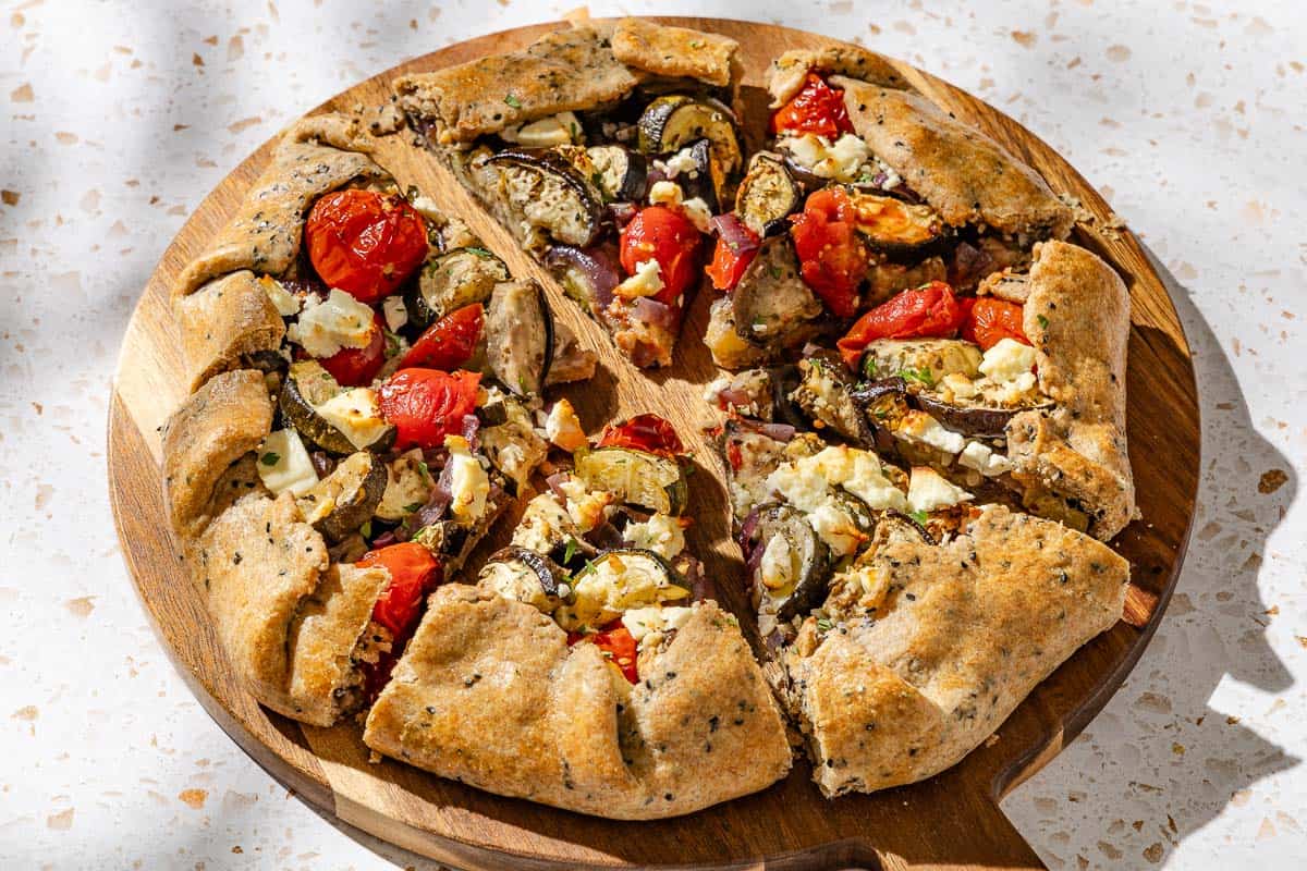 A close up of a savory galette cut into slices on a wooden serving board.