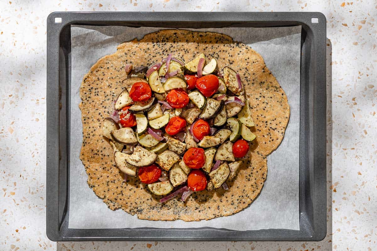 An overhead photo of the unbaked savory galette on a parchment lined baking sheet before the edges of the dough are folded over the edge of the roasted vegetables.