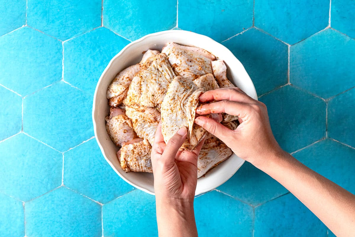 An over head phot of bone in, skin on chicken thighs being seasoned with the za'atar garlic sauce.