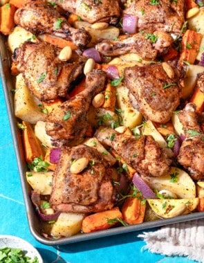 A close up photo of sheet pan za'atar chicken with veggies next to a small bowl of chopped parsley.