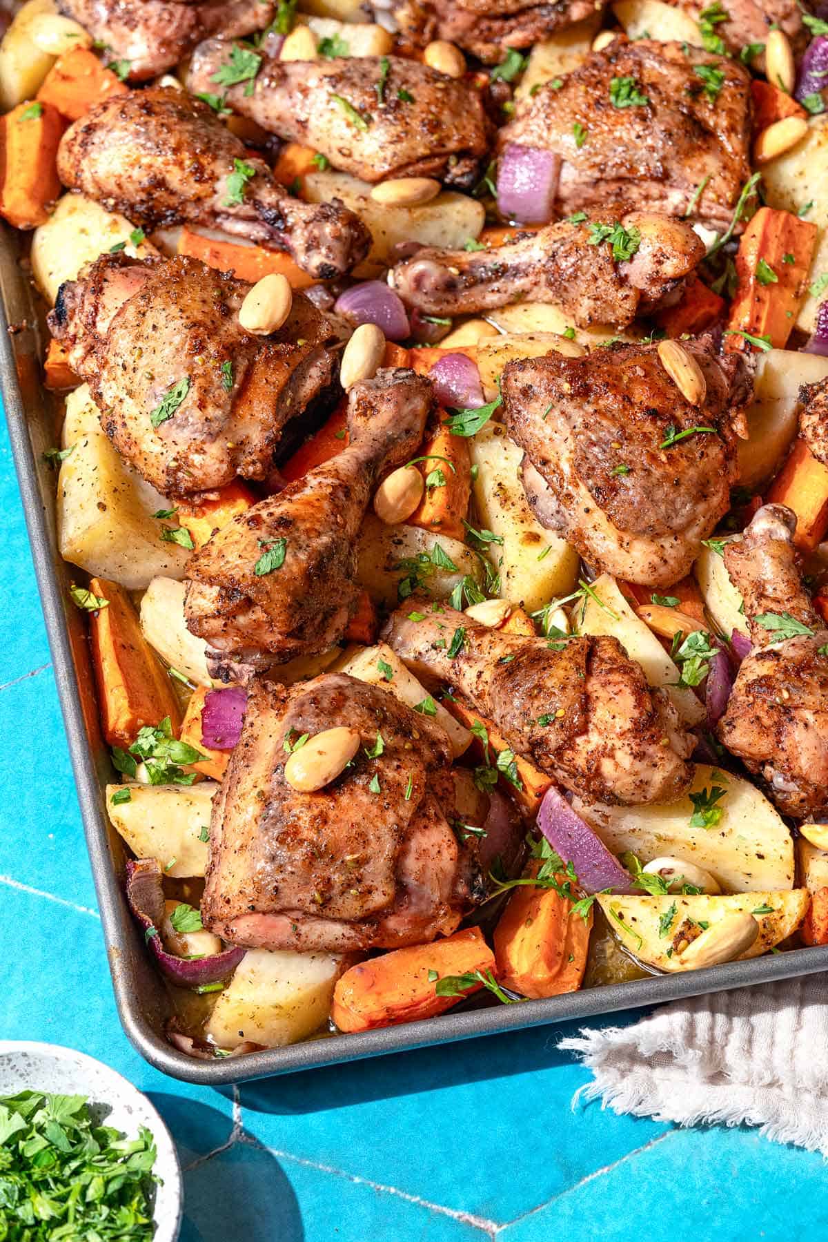 A close up photo of sheet pan za'atar chicken with veggies next to a small bowl of chopped parsley.