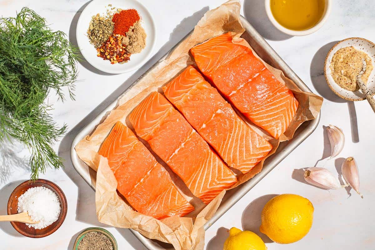 Ingredients for baked dijon salmon including salmon fillets, olive oil, lemons, dijon mustard, garlic, oregano, coriander, paprika, red pepper flakes, salt, black pepper and dill.