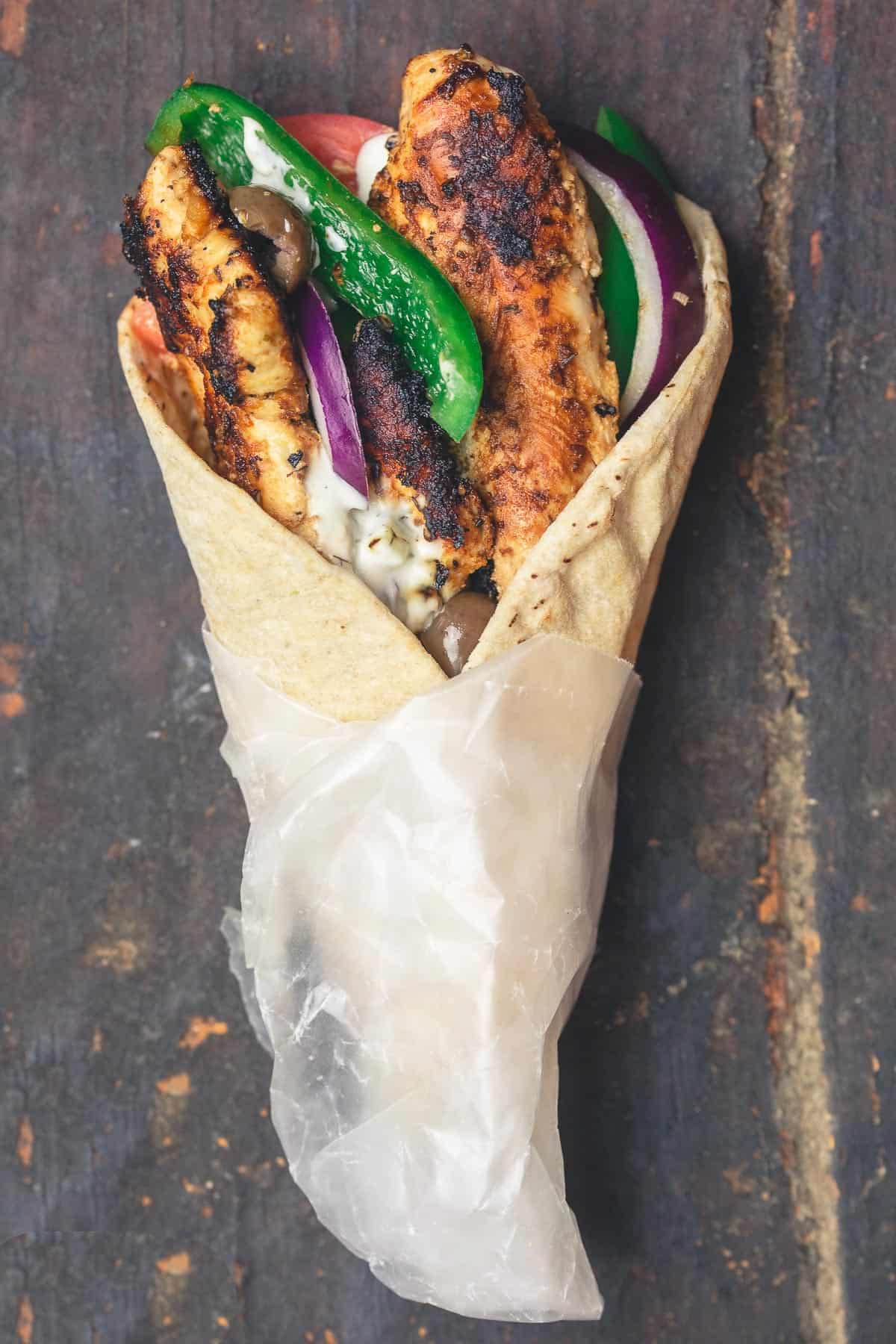 A chicken gyro wrap with tomatoes, onions, green peppers and olives.