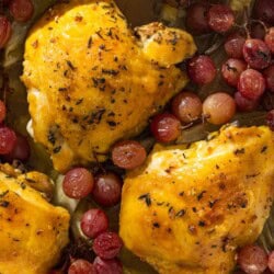 An overhead photo of 3 braised chicken thighs in a baking dish with grapes and fennel.