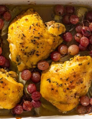 An overhead photo of 3 braised chicken thighs in a baking dish with grapes and fennel.