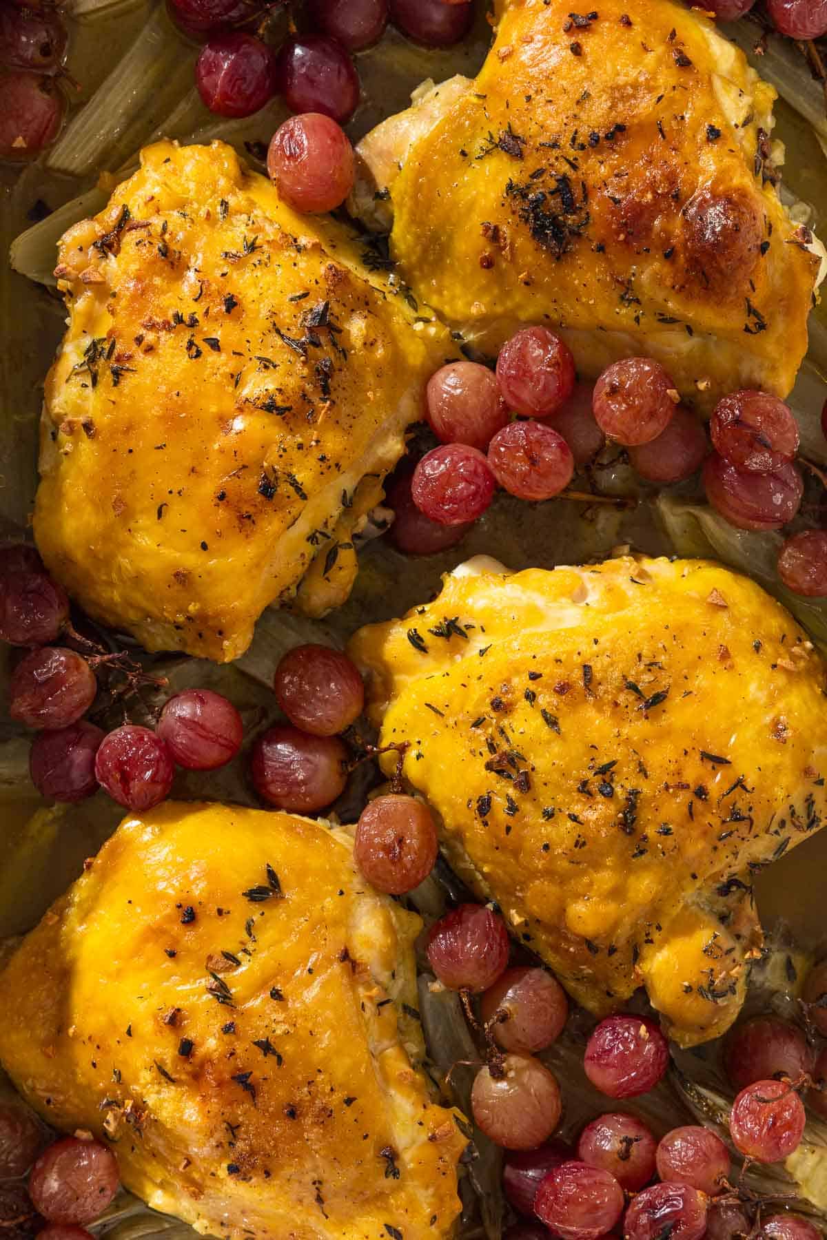 An overhead photo of 4 braised chicken thighs with grapes and fennel.