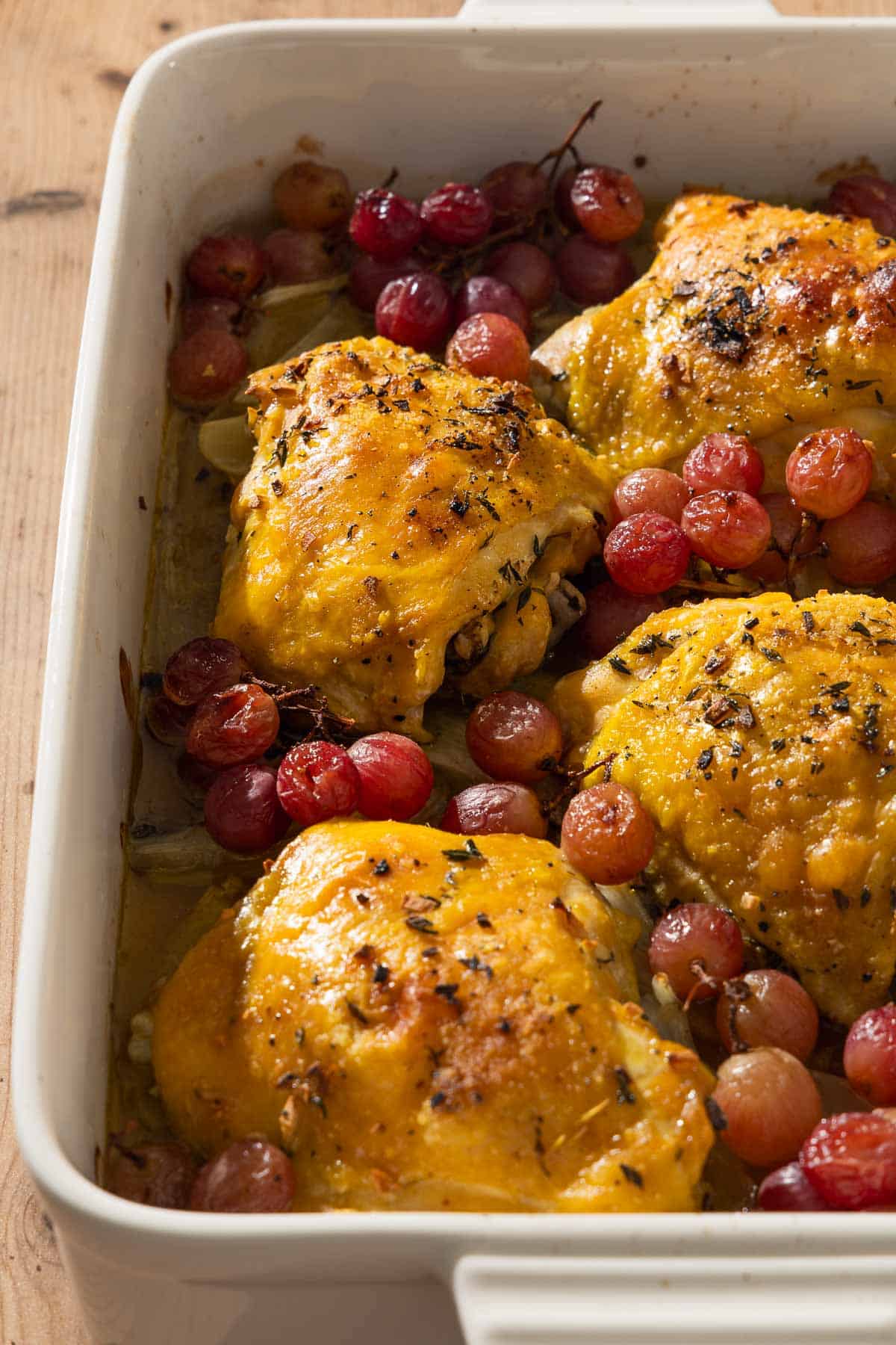 A close up of 4 braised chicken thighs in a baking dish with grapes and fennel.