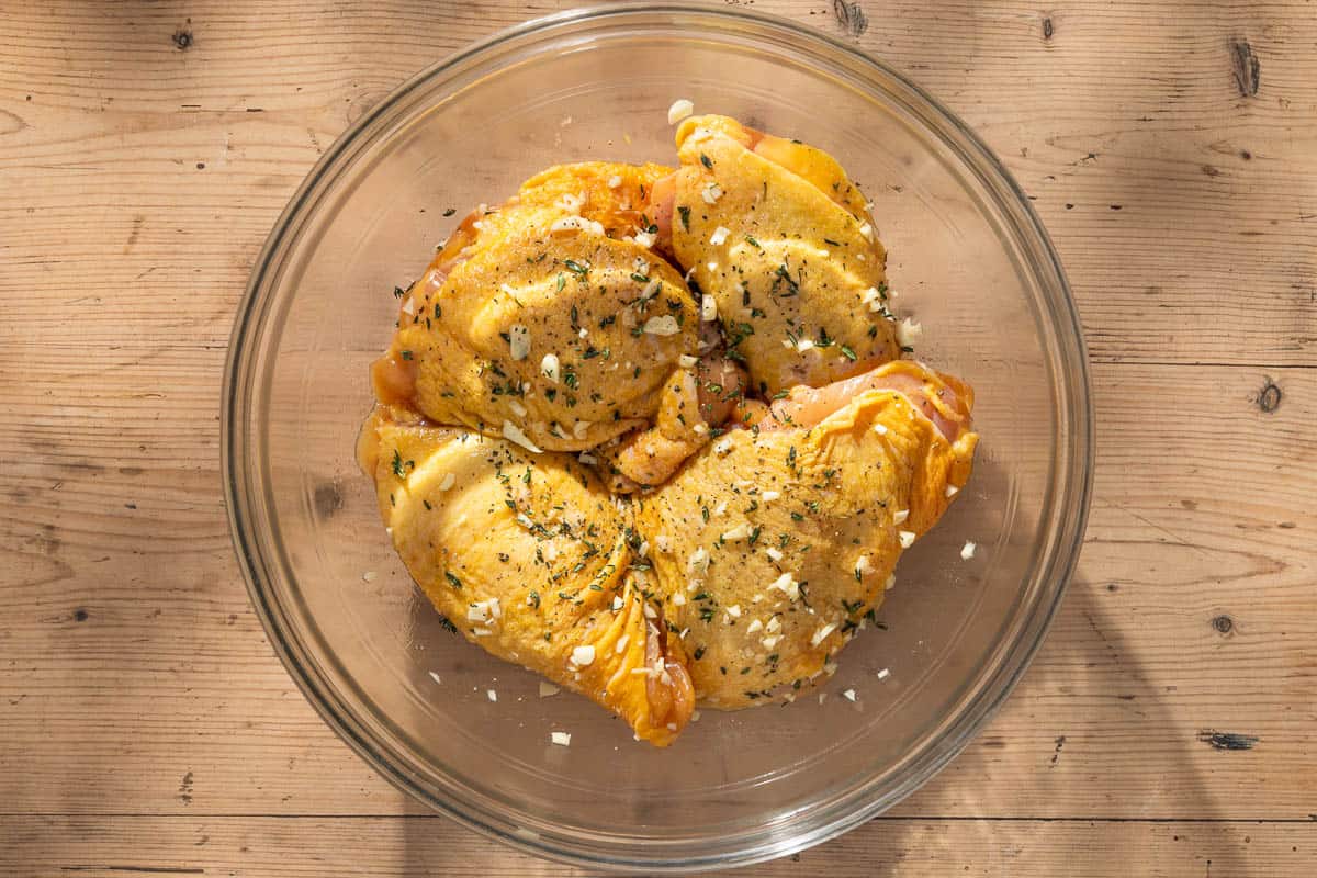 An overhead photo of 4 uncooked, seasoned chicken thighs in a large bowl.