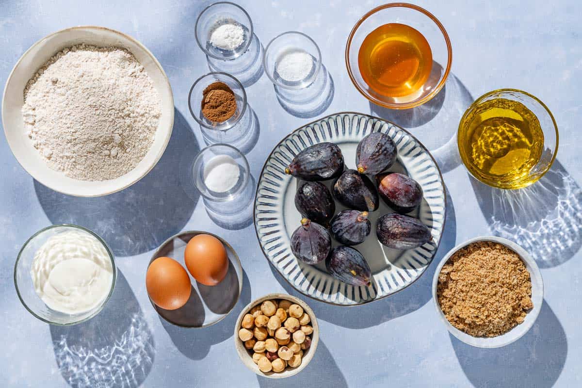 Ingredients for whole wheat fig bread including white whole wheat flour, baking soda, baking powder, salt, cinnamon, olive oil, brown sugar, honey, eggs, greek yogurt, vanilla extract, figs and hazelnuts.