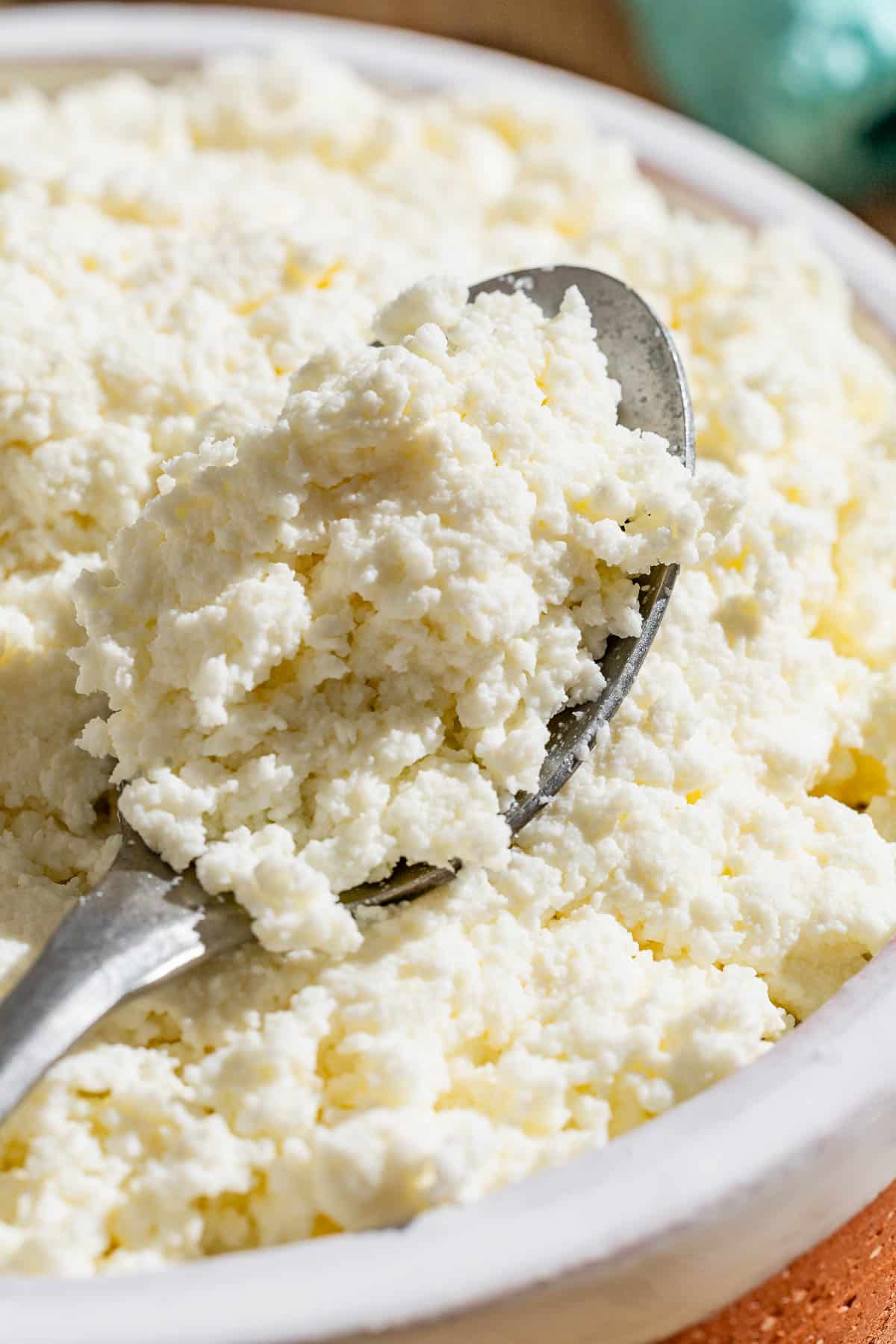 A close up of homemade ricotta in a bowl with a spoon.