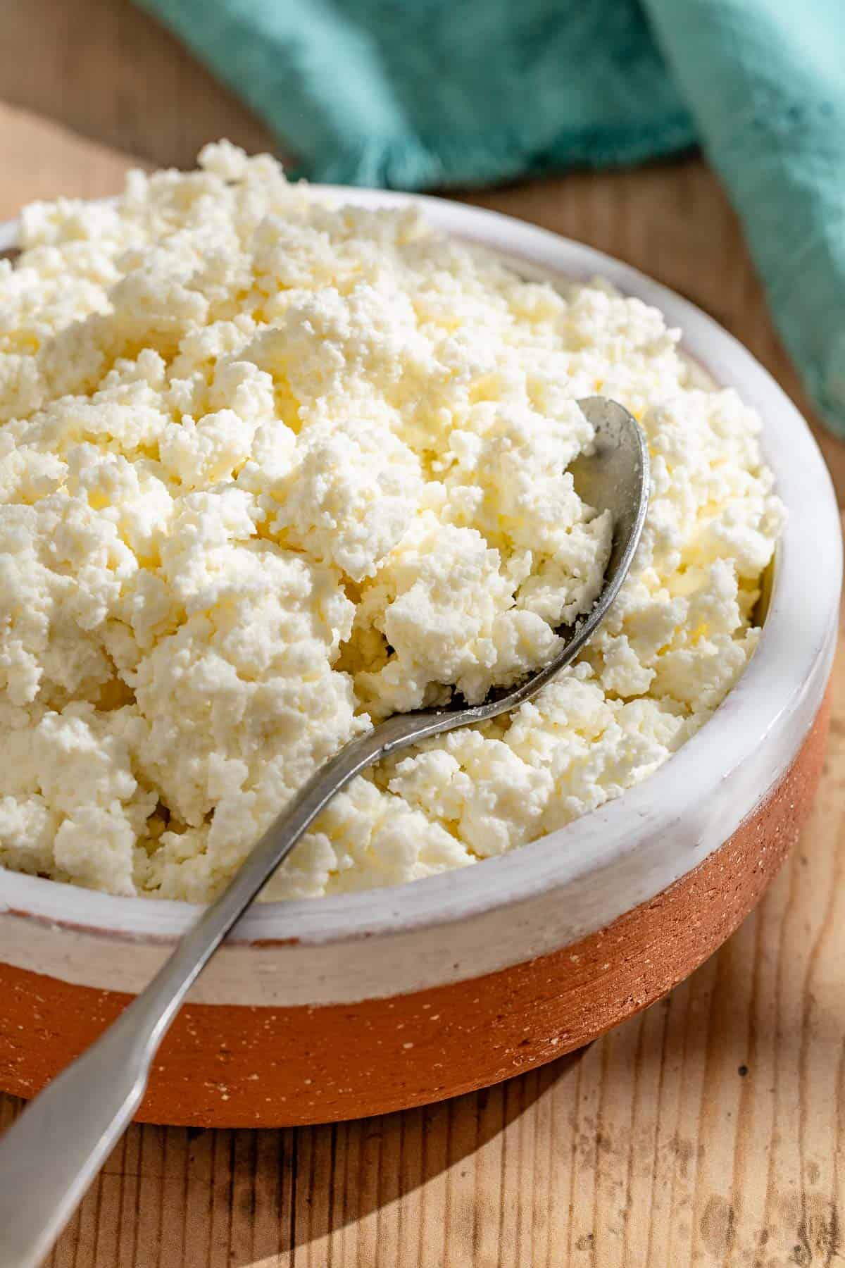 A close up of homemade ricotta in a bowl with a spoon.