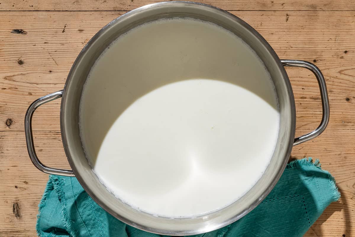 An overhead photo of milk in a large pot next to a kitchen towel.