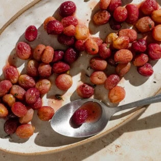 An overhead photo of roasted grapes with sherry and thyme on a plate with a spoon.