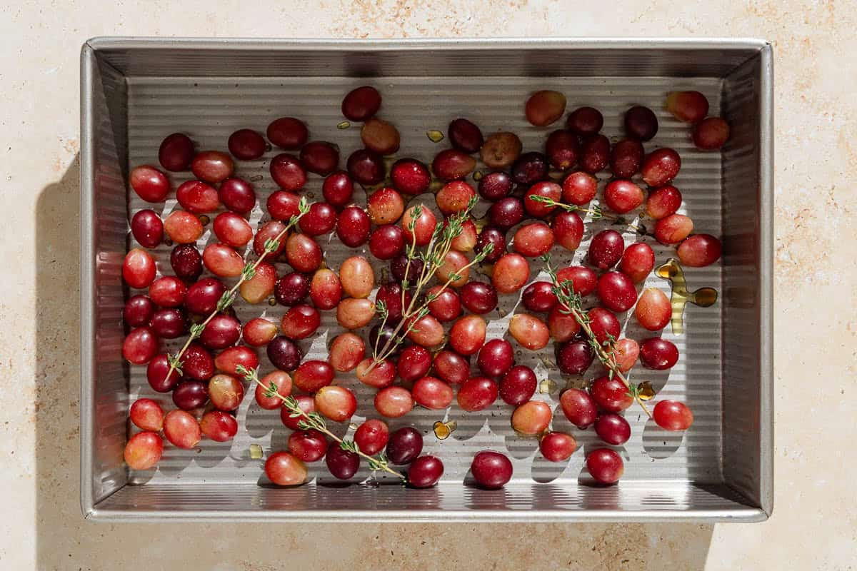 An overhead photo of grapes with sherry and thyme in a baking pan before being roasted.