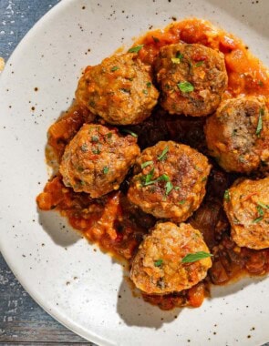 An overhead photo of a serving of Spanish meatballs and sauce on a plate. Next to this is a slice of bread and a glass of red wine.