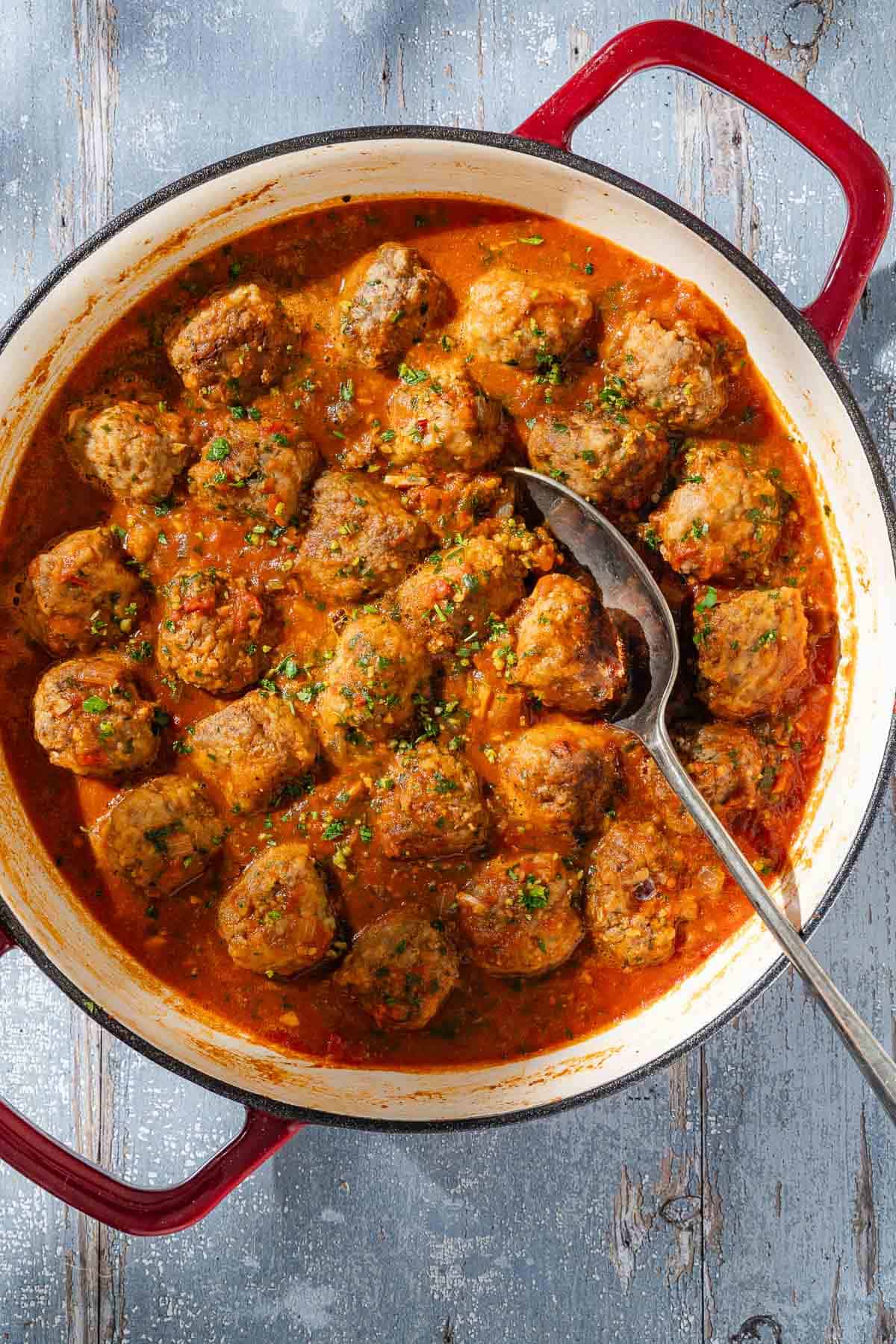 An overhead photo of Albóndigas (Spanish meatballs) with sauce in a dutch oven with a serving spoon.