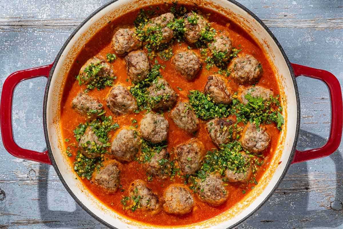 An overhead photo of the Spanish meatballs simmering in sauce and topped with the picada in a skillet.