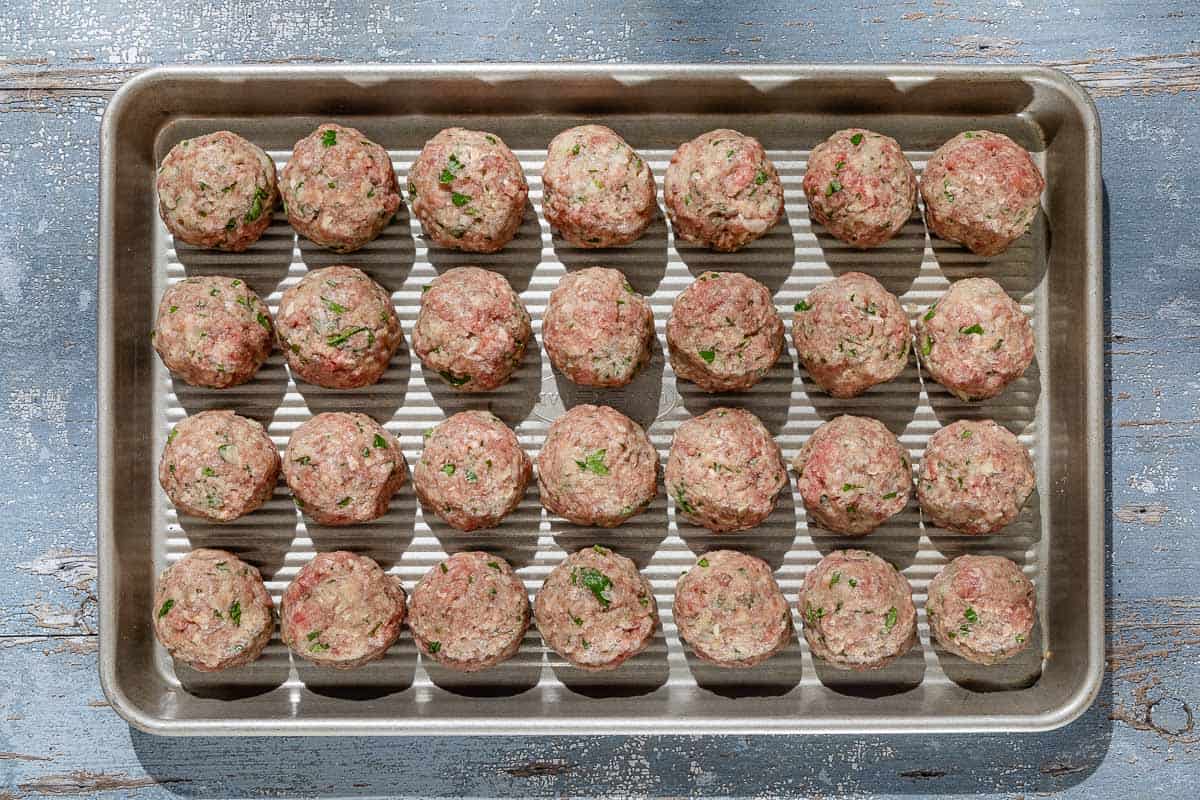 An overhead photo of unbaked Spanish meatballs spread evenly on a baking sheet.