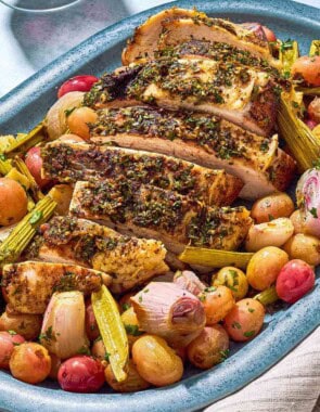 A close up photo of a sliced roast turkey breast with grapes and vegetables on a serving platter.