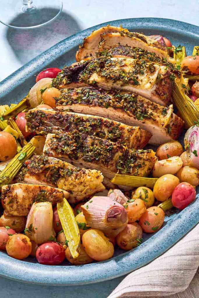 A close up photo of a sliced roast turkey breast with grapes and vegetables on a serving platter.