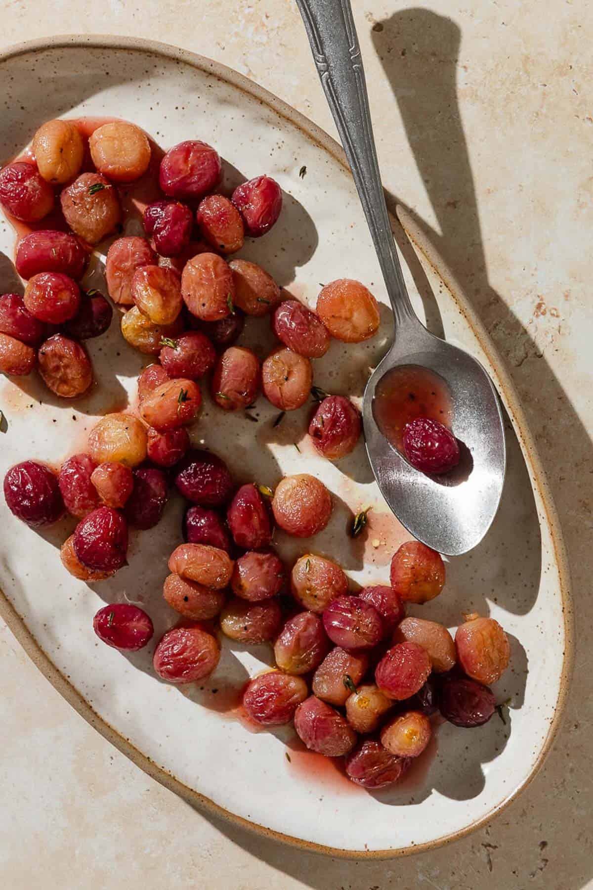 An overhead photo of roasted grapes with sherry and thyme on a plate with a spoon.