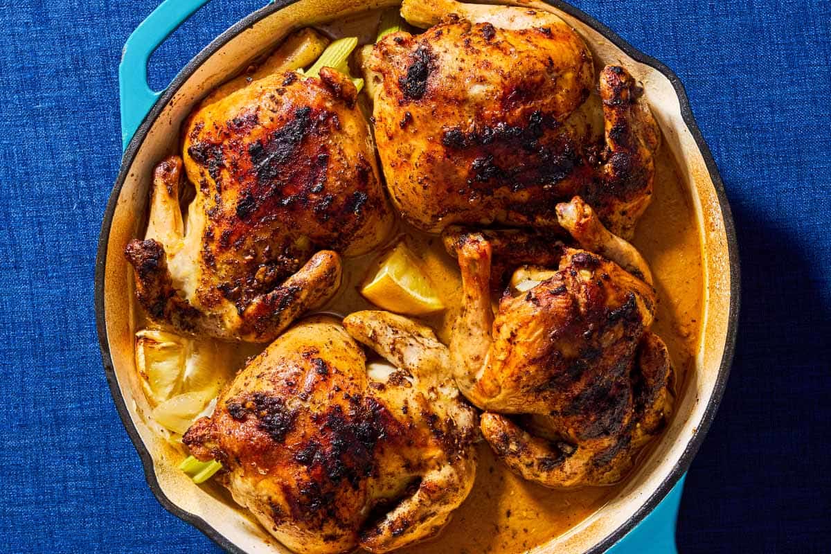 An overhead photo of 4 roasted cornish hens in a large skillet with lemon wedges.