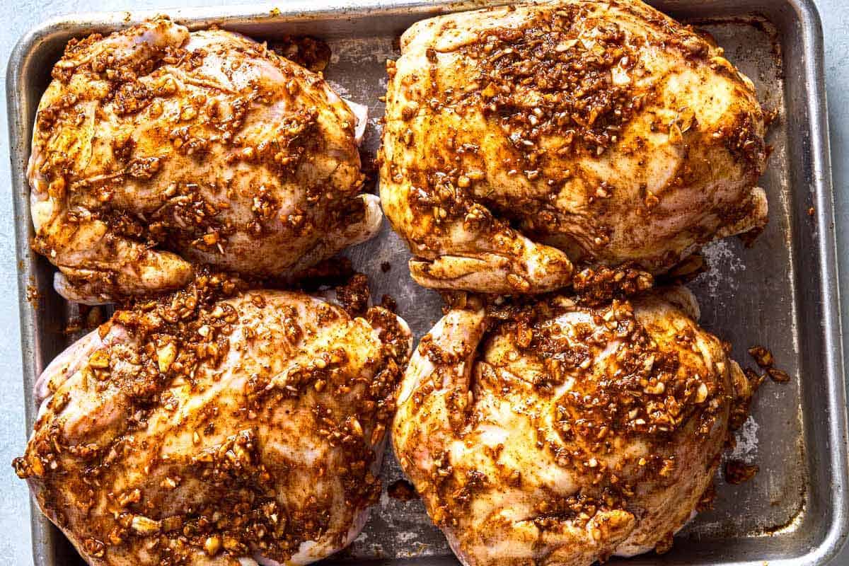 4 marinated cornish hens on a baking sheet.