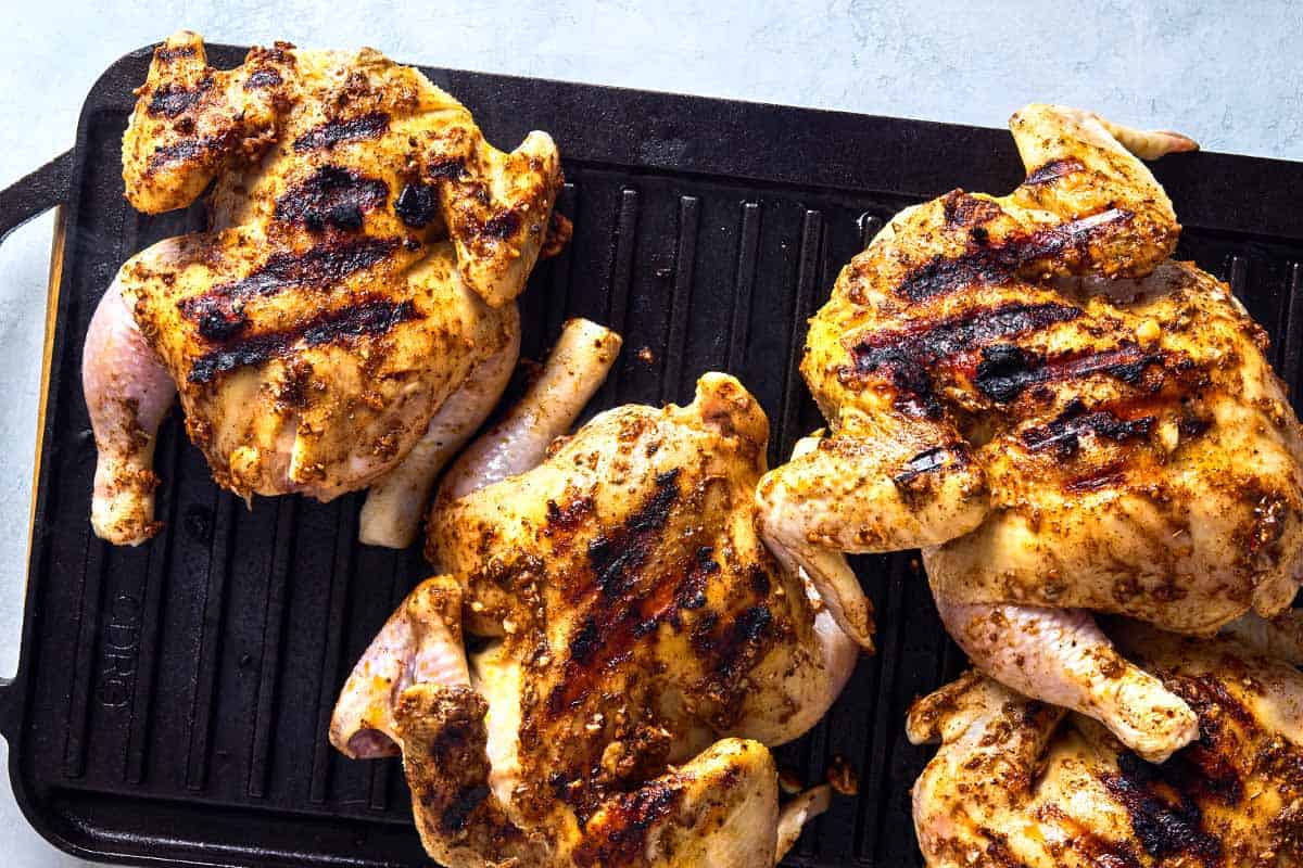 An overhead photo of 4 cornish hens being browned on a cast iron grill.