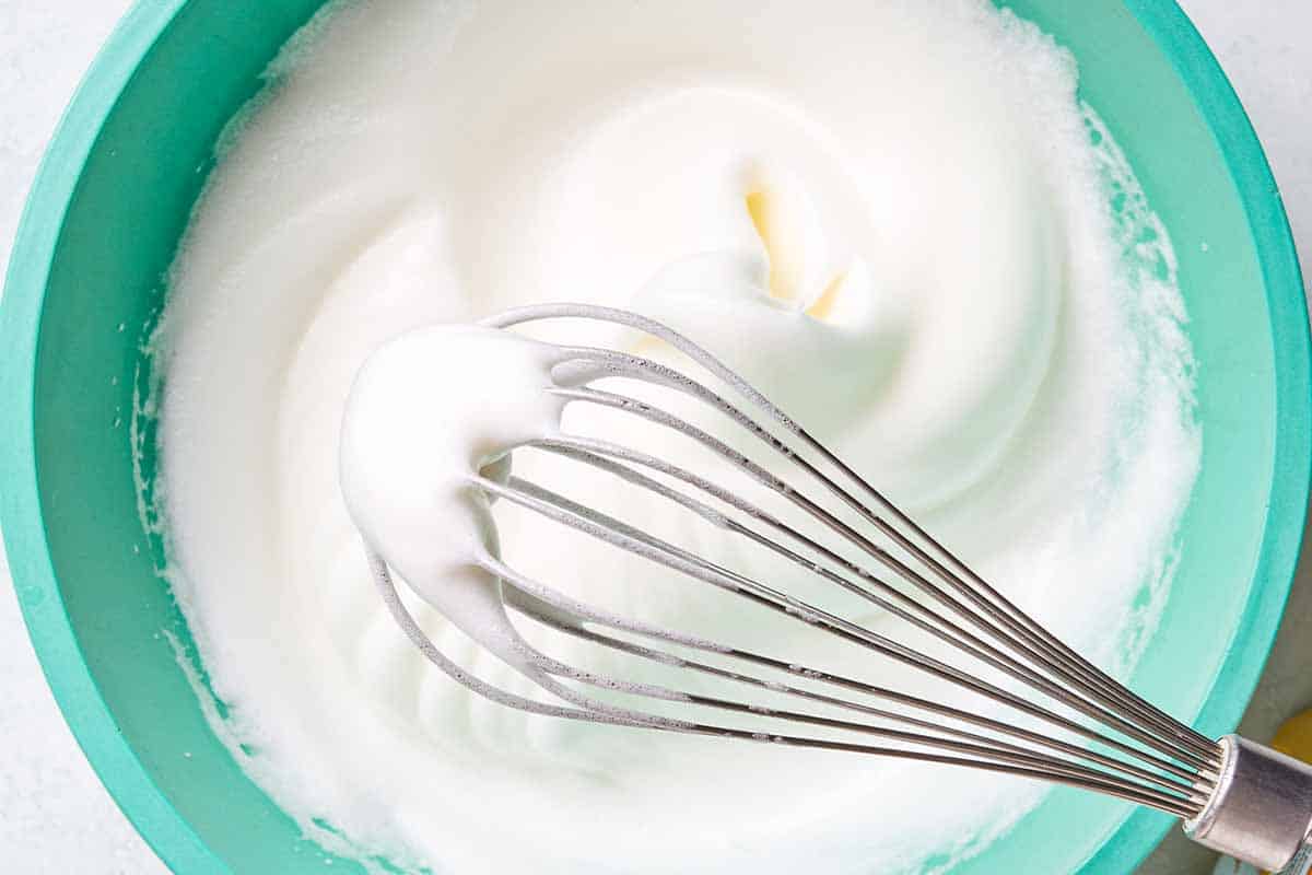 An overhead close up photo the egg whites for the flourless chocolate cake in a mixing bowl with a whisk after they've been beaten until frothy.