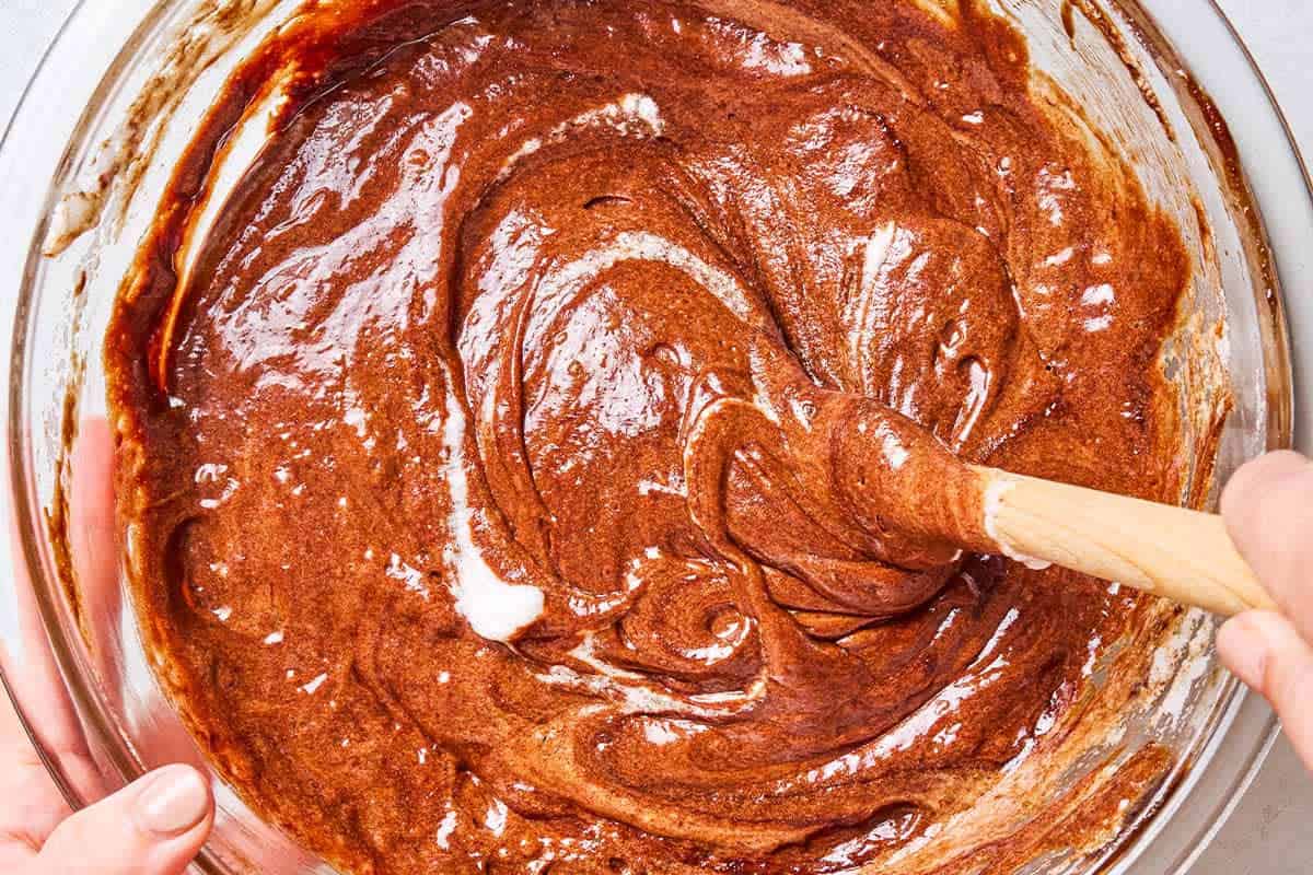 An overhead close up photo of the batter for the flourless chocolate cake in a mixing bowl being stirred with a wooden spoon.