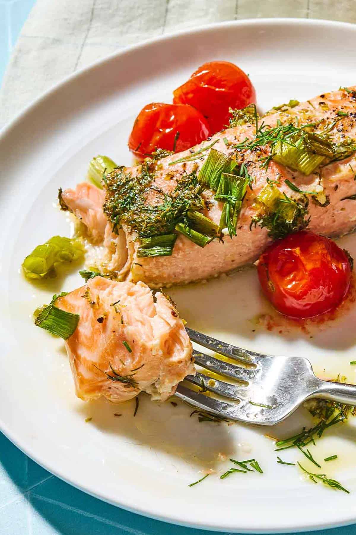 A close up of a greek salmon fillet on a plate with a fork and some cherry tomatoes.