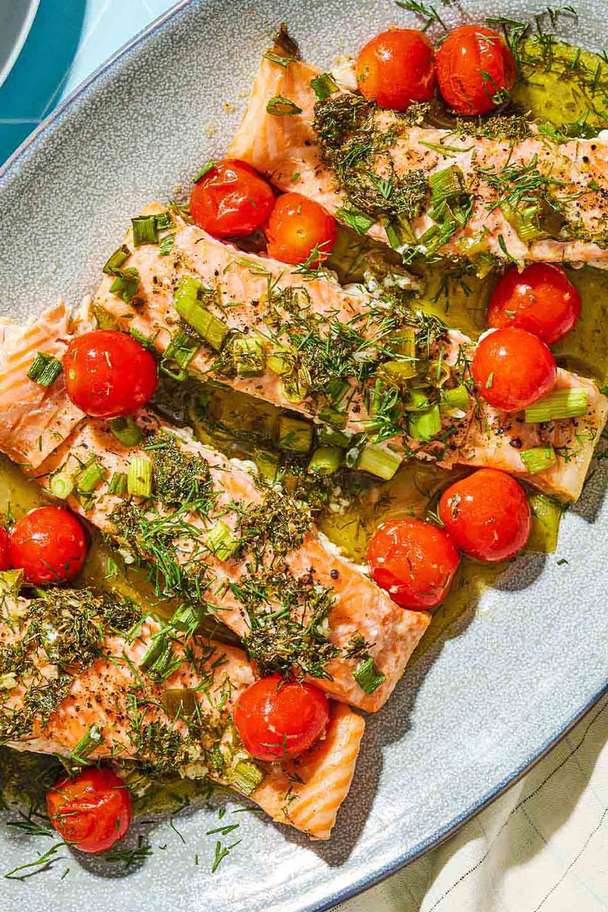 A close up of 4 Greek salmon fillets with cherry tomatoes on a platter.