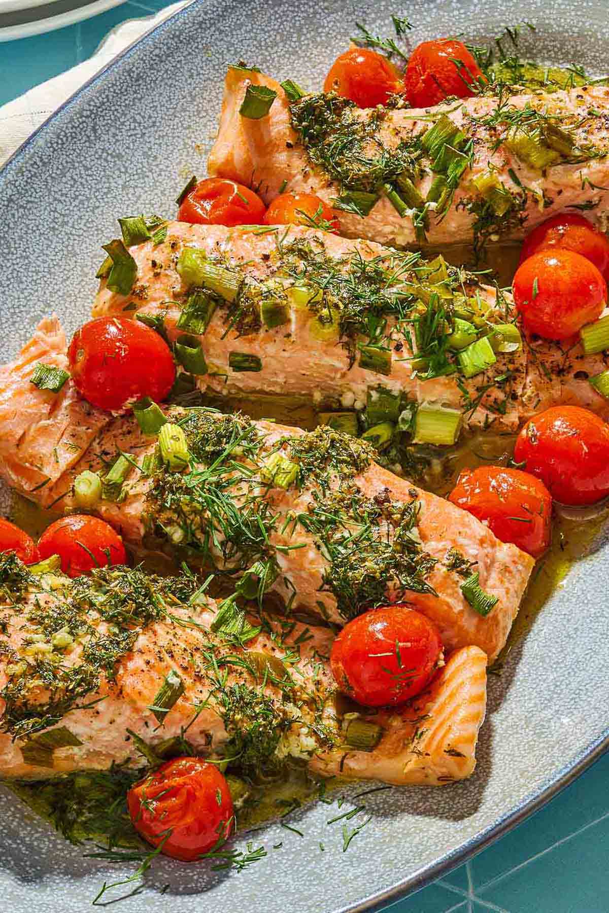 A close up of 4 Greek salmon fillets with cherry tomatoes on a platter.