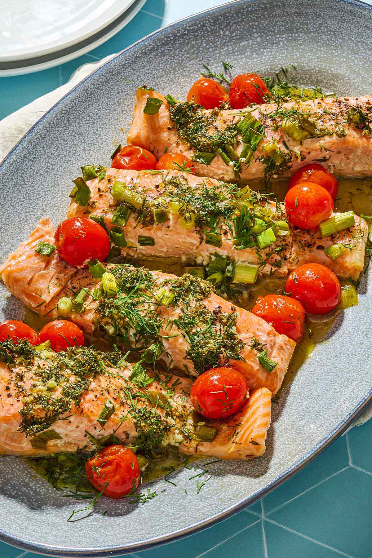 4 Greek salmon fillets with cherry tomatoes on a platter.