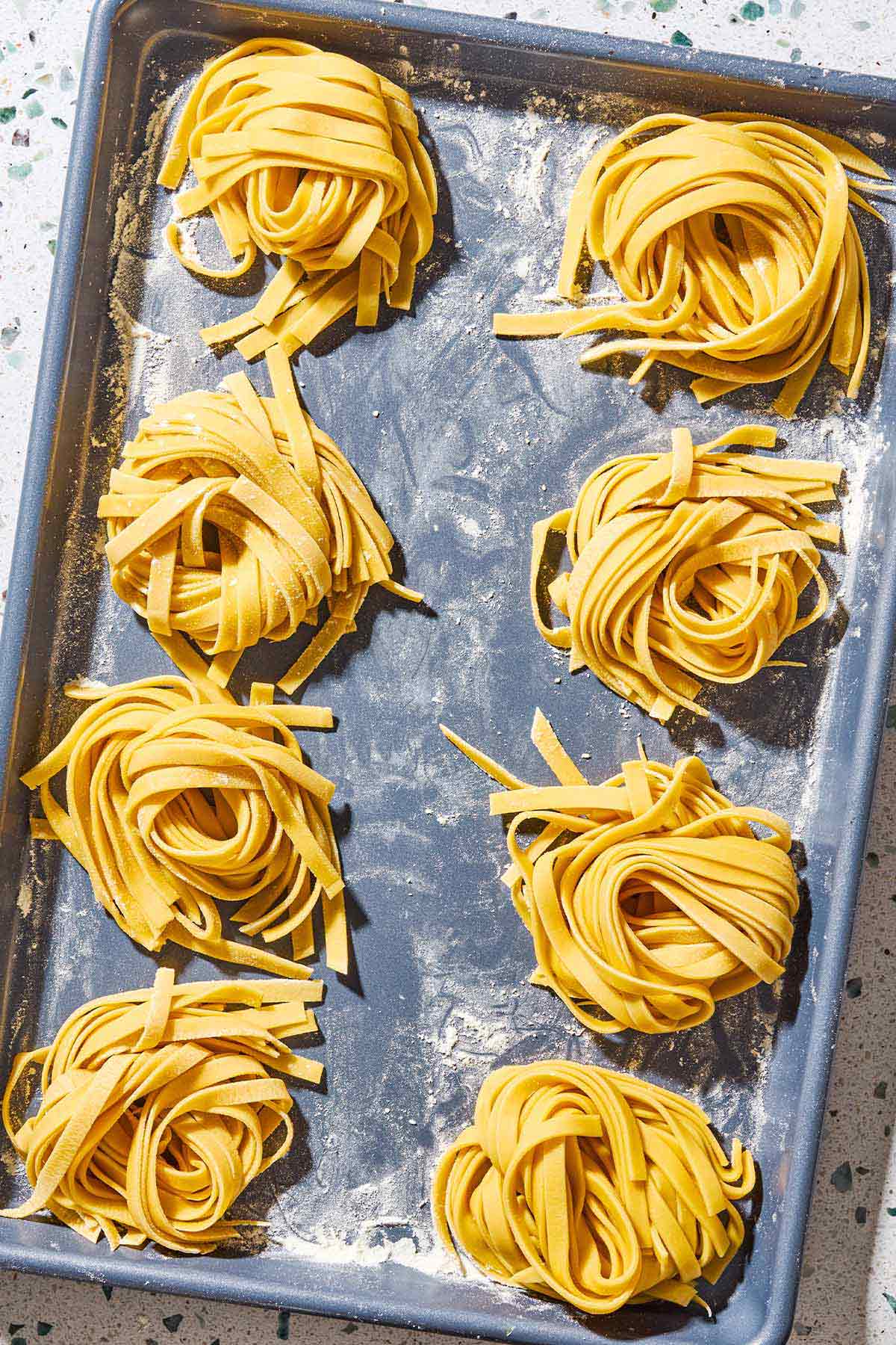 An overhead photo of uncooked homemade pasta noodles formed into 8 nest shapes.