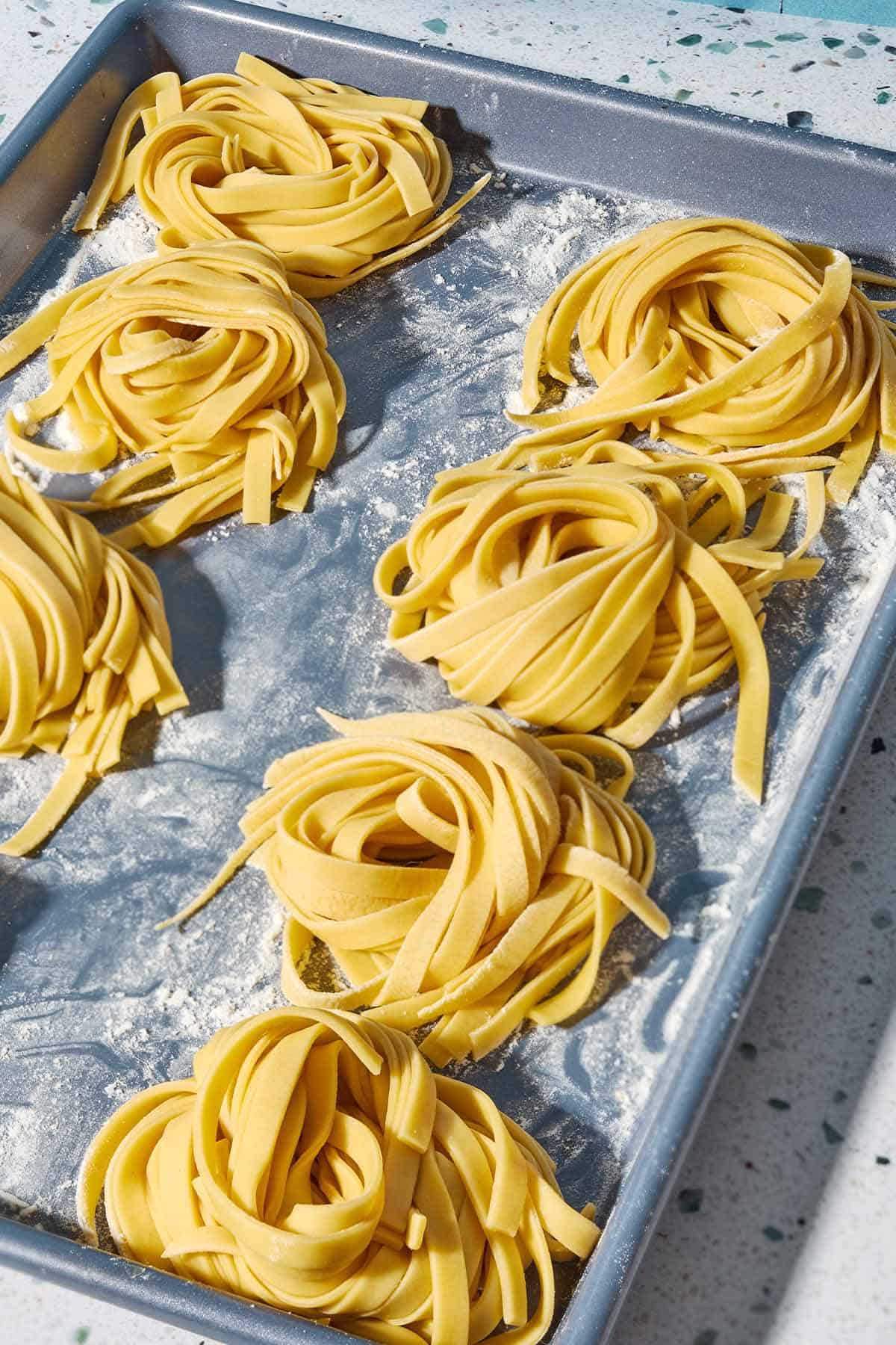 A close up photo of uncooked homemade pasta noodles formed into several nest shapes.