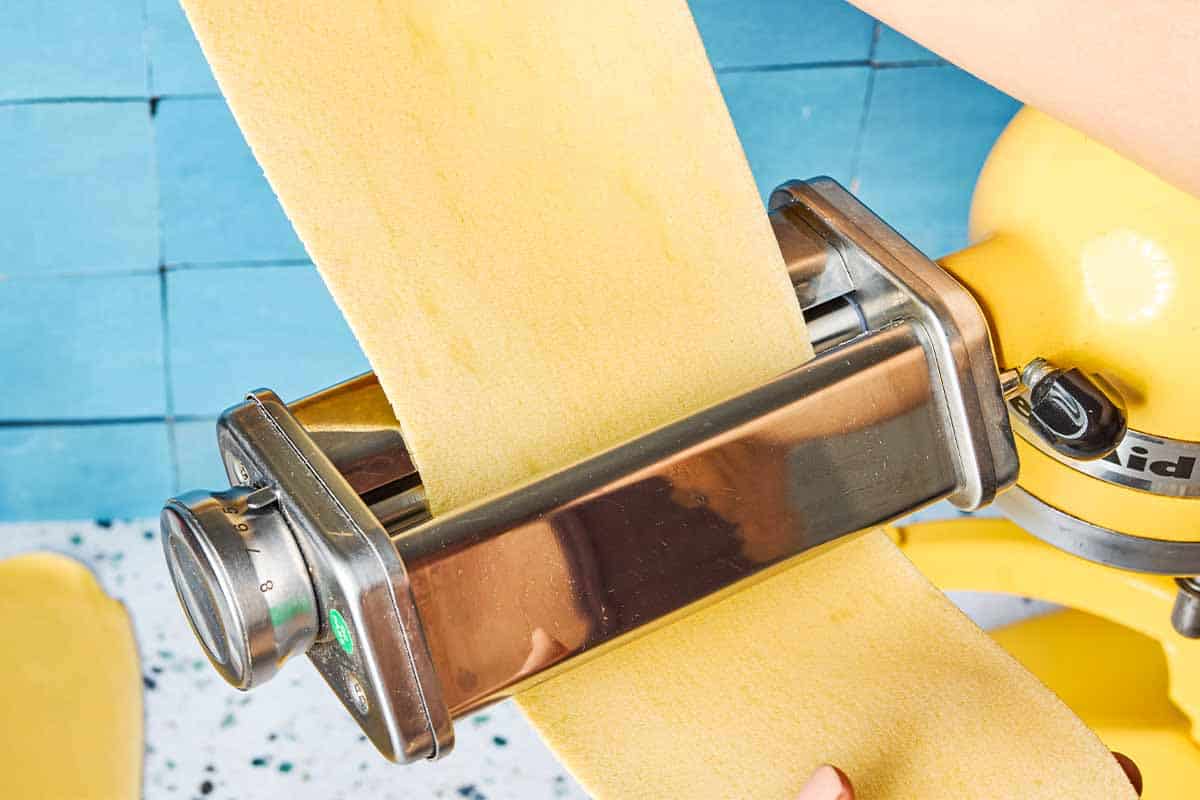 A close up of a sheet of pasta dough being stretched through the rollers of a pasta machine.