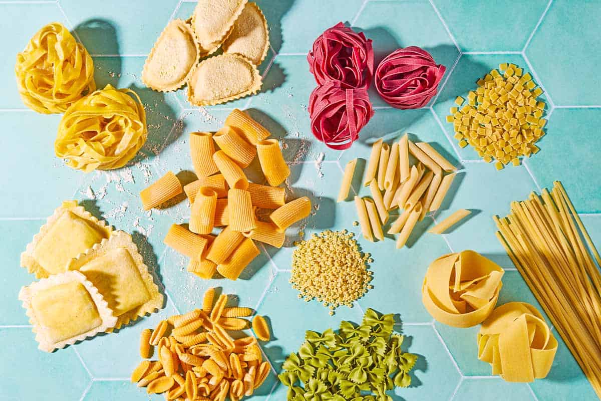 An overhead photo a a variety of uncooked pasta shapes.