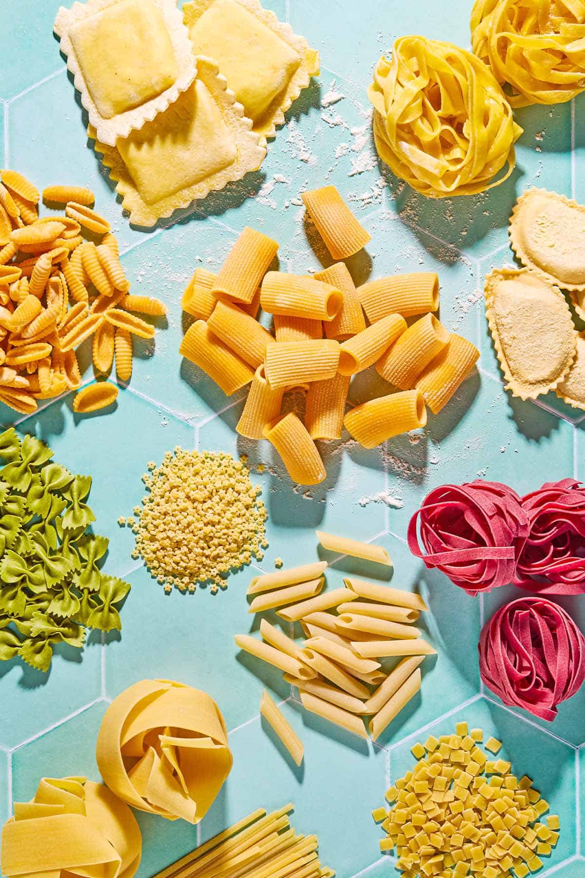 An overhead photo a a variety of uncooked pasta shapes.