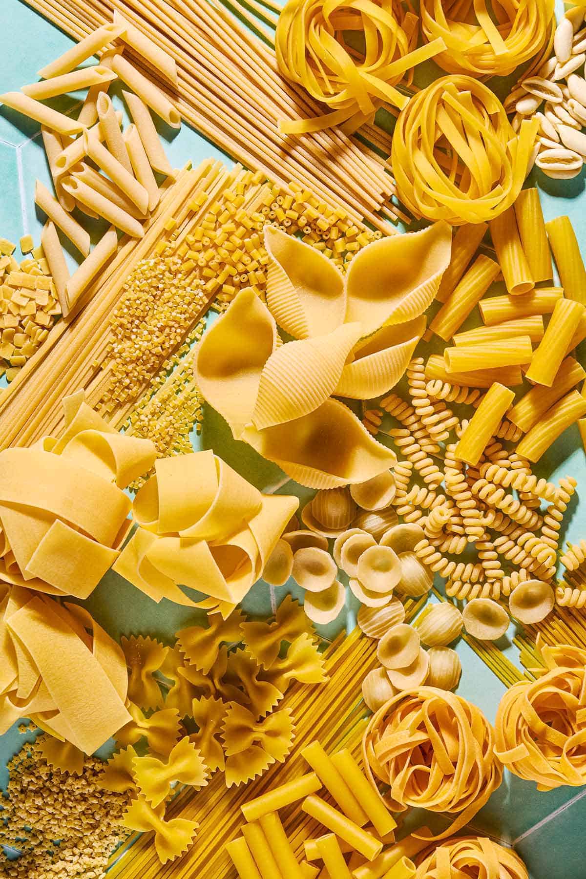 An overhead photo a a variety of uncooked pasta shapes.