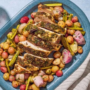 An overhead photo of a sliced roast turkey breast with grapes and vegetables on a serving platter. Next to this is a cloth napkin and glasses of red wine.