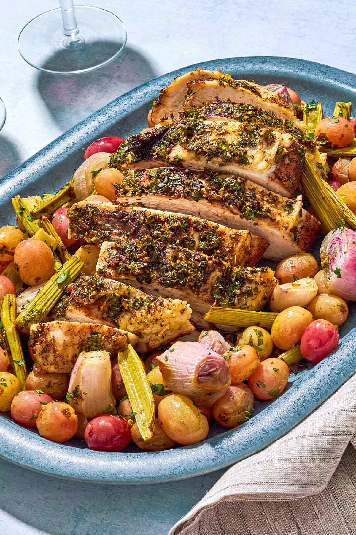 A close up of a sliced roast turkey breast with grapes and vegetables on a serving platter.