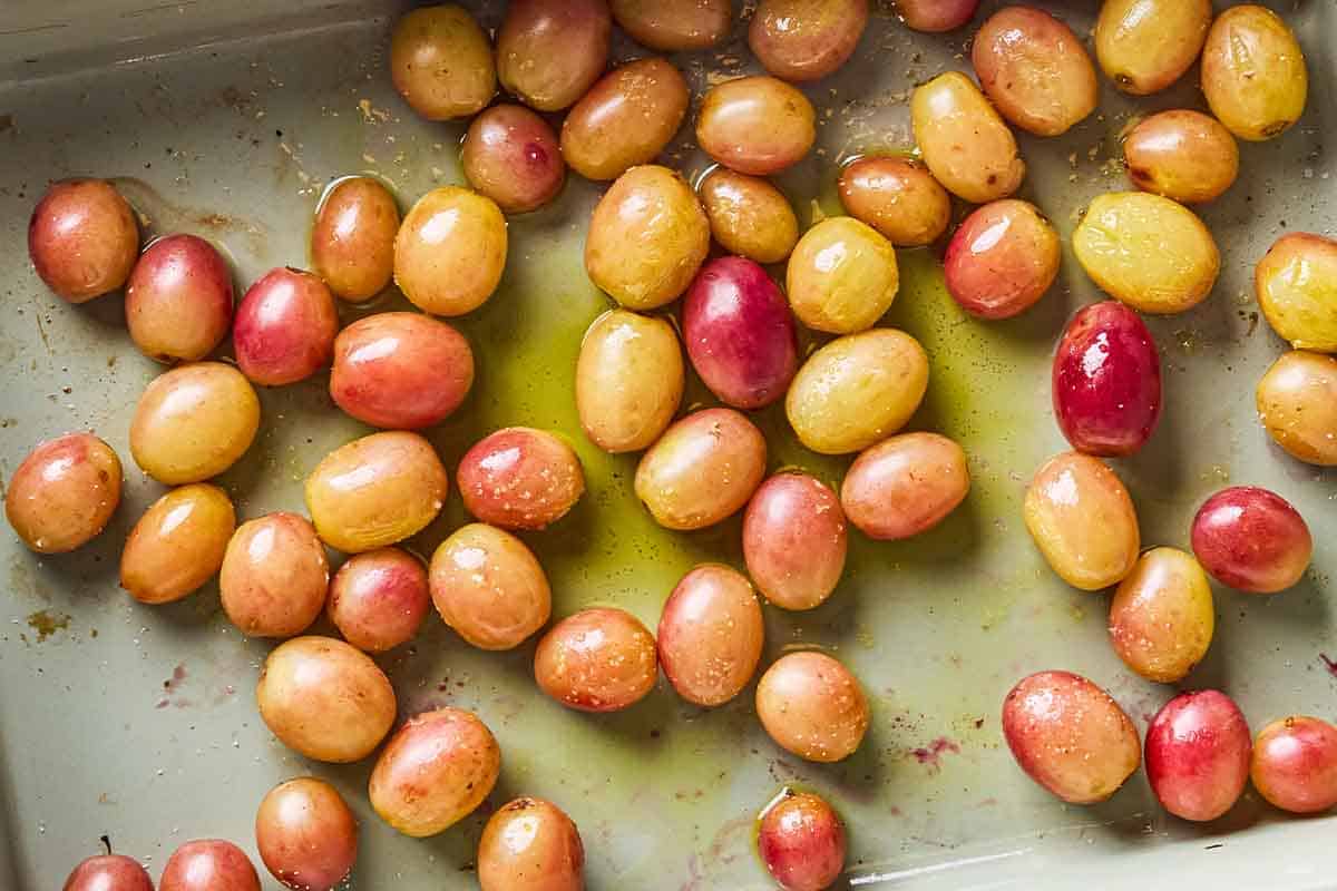 An close up of red grapes, seasoned with salt and drizzled with oil in a baking dish.