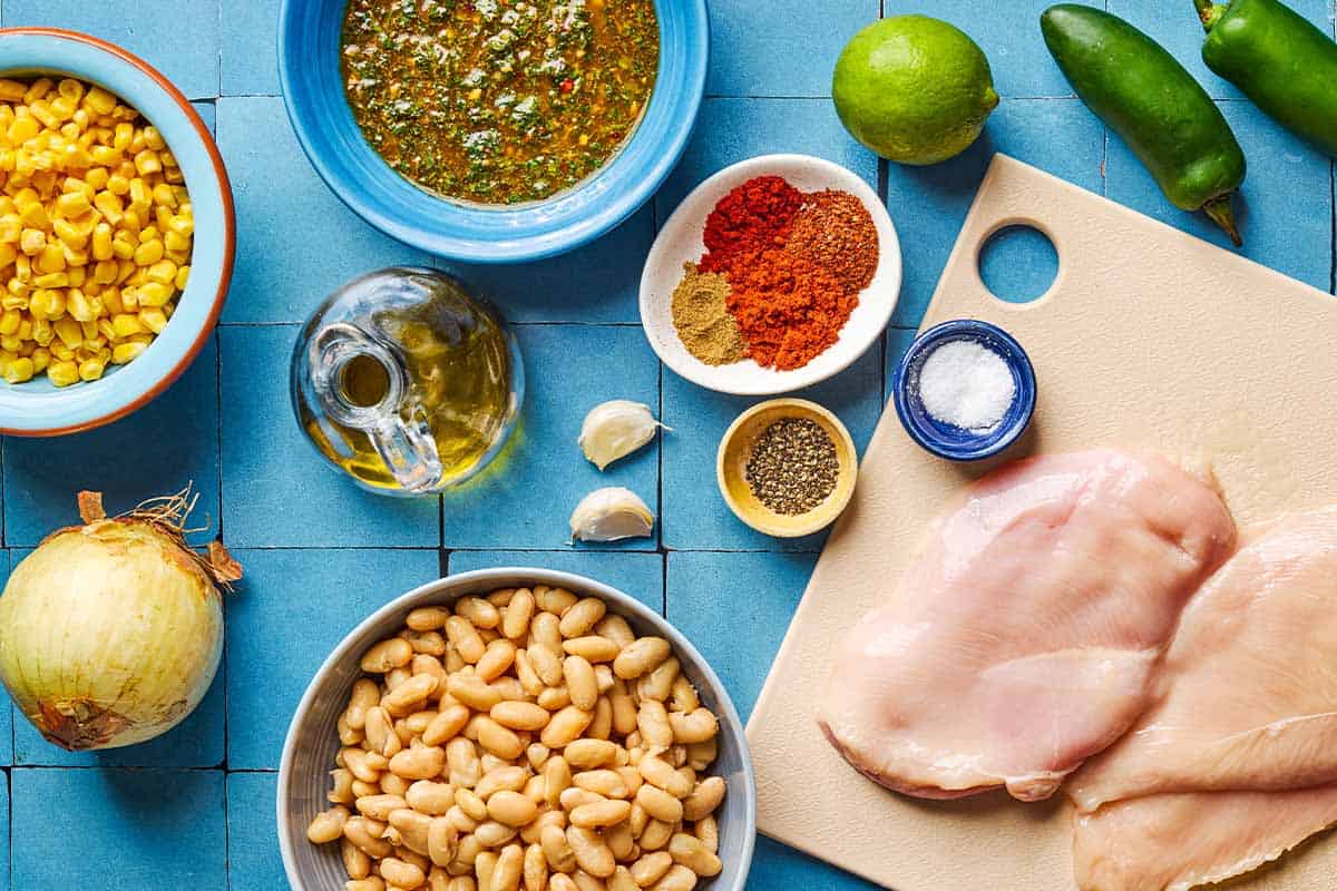 Ingredients for white chicken chili including chicken, olive oil, onion, garlic, salt, black pepper, chili powder, cumin, smoked paprika, aleppo pepper, cannellini beans, corn, lime, jalapeno peppers and chermoula.