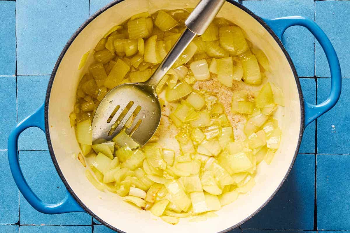 An overhead photo of chopped onion and garlic being sauteed in a pot with a slotted spoon.