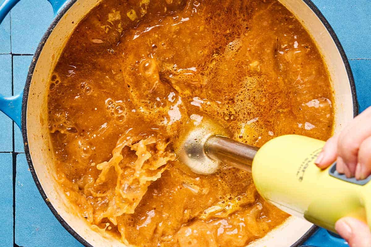 An overhead photo of an immersion blender being used to slightly blend the white chicken chili in a pot.