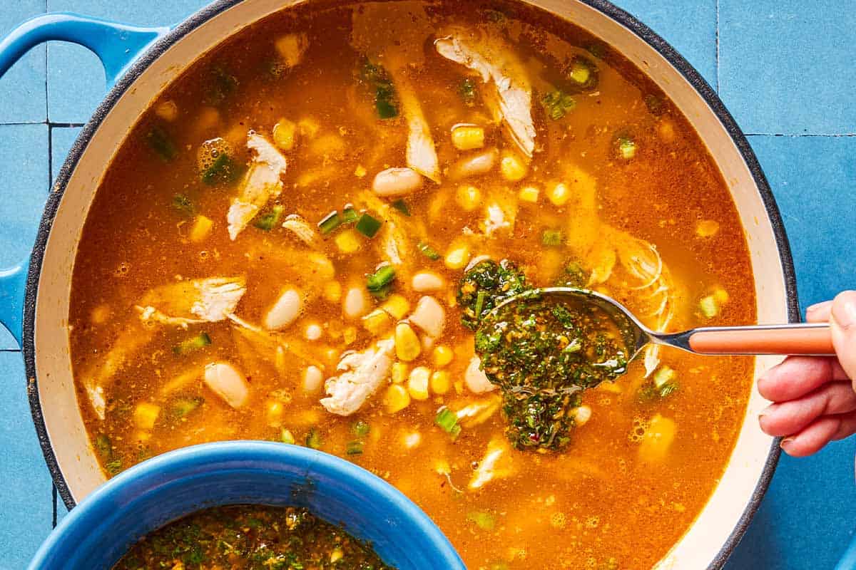 An overhead photo of white chicken chili in pot being topped with chermoula with a spoon.